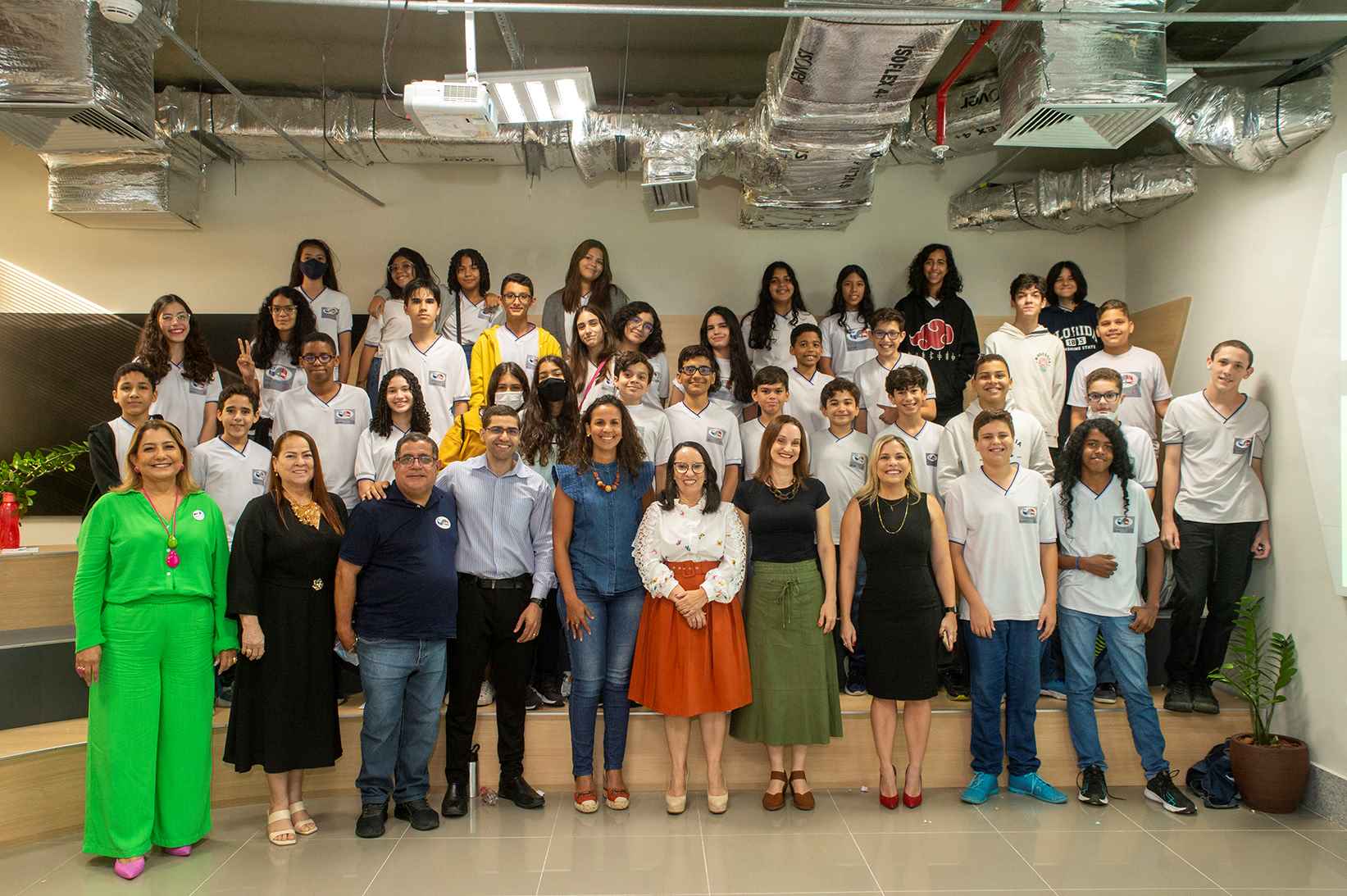 Grupo de pessoas de pé em uma sala espaçosa posam para foto sorridentes