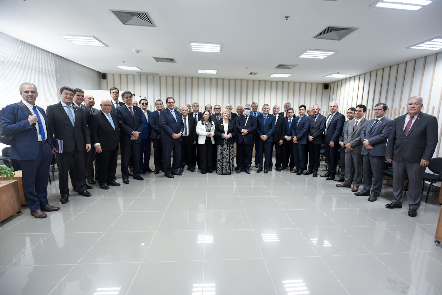 Foto mostra grupo de pessoas em uma sala, todos de pé, lado a lado.