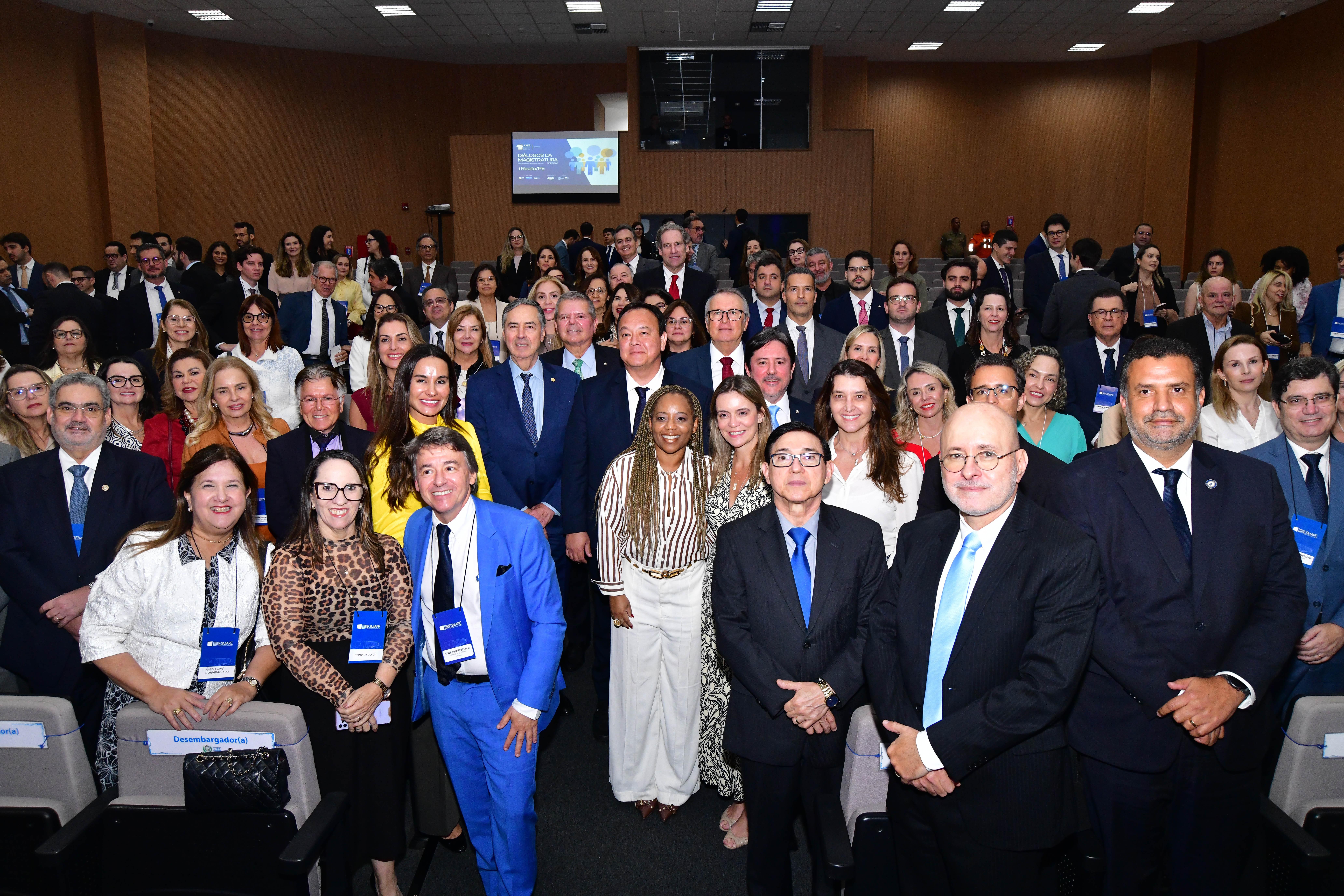 Final do evento, todos estão de pé no auditório virados para a câmera