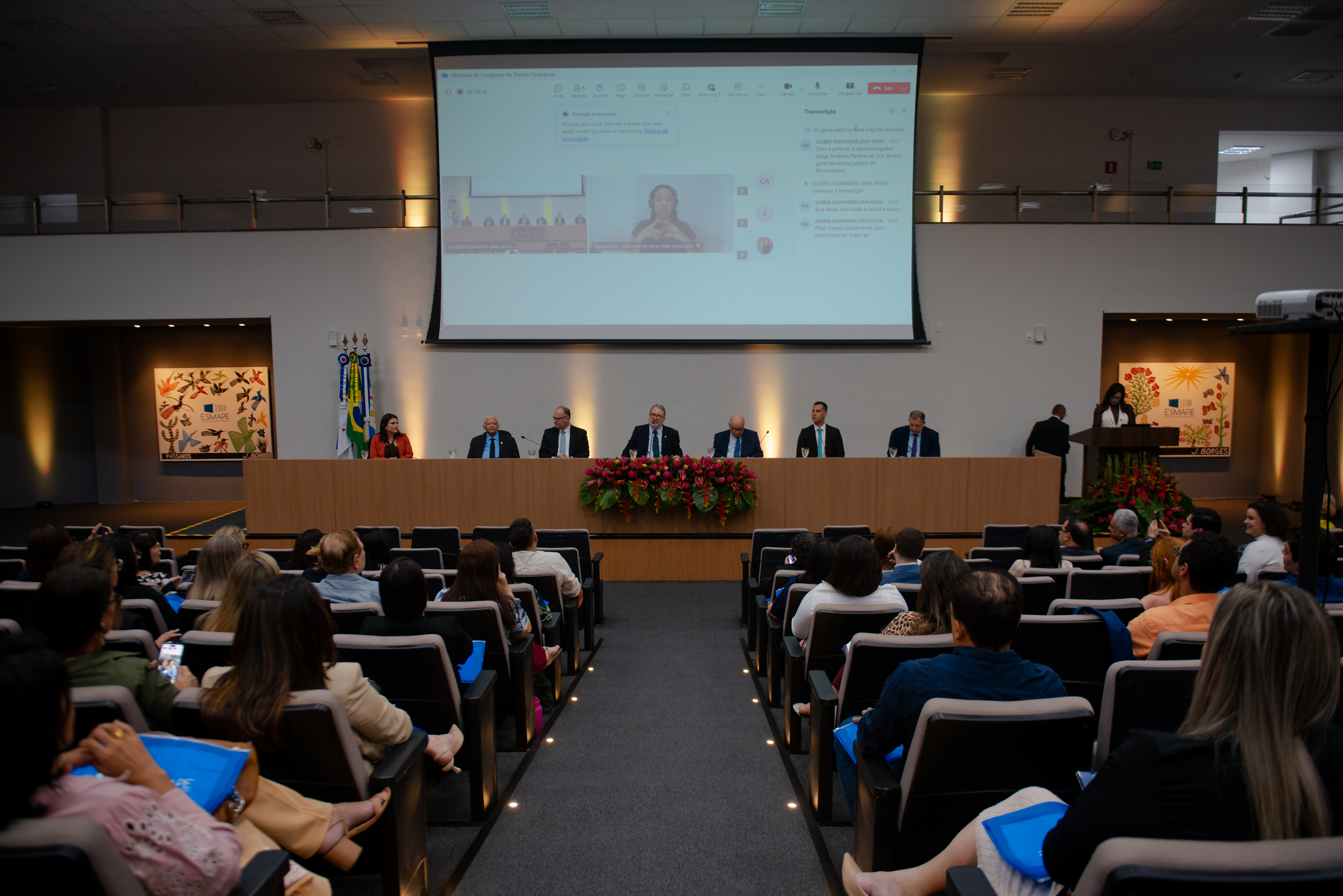 Seis homens e uma mulher sentados atrás de uma grande mesa de frente para um auditório.