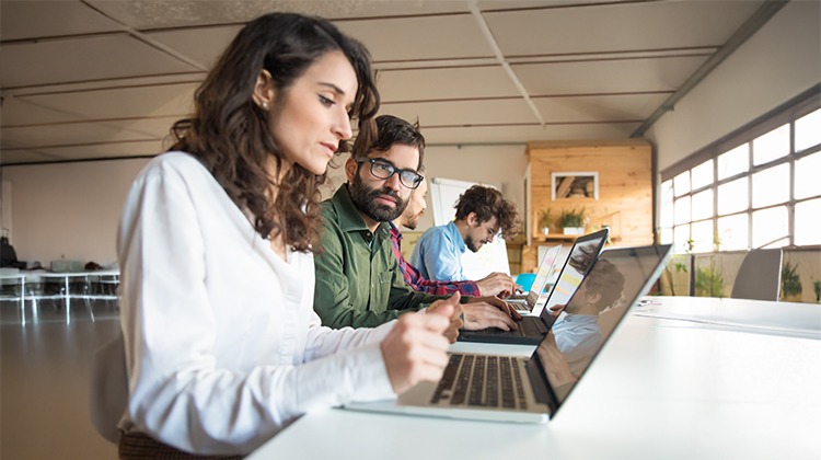 Três pessoas sentadas à mesa usando laptops