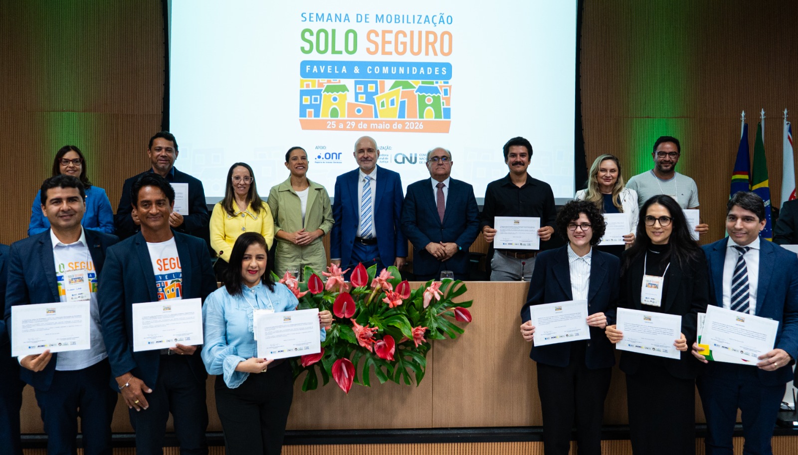 Pessoas que receberam certificado na ocasião, todos em pé posicionados na frente da mesa de honra
