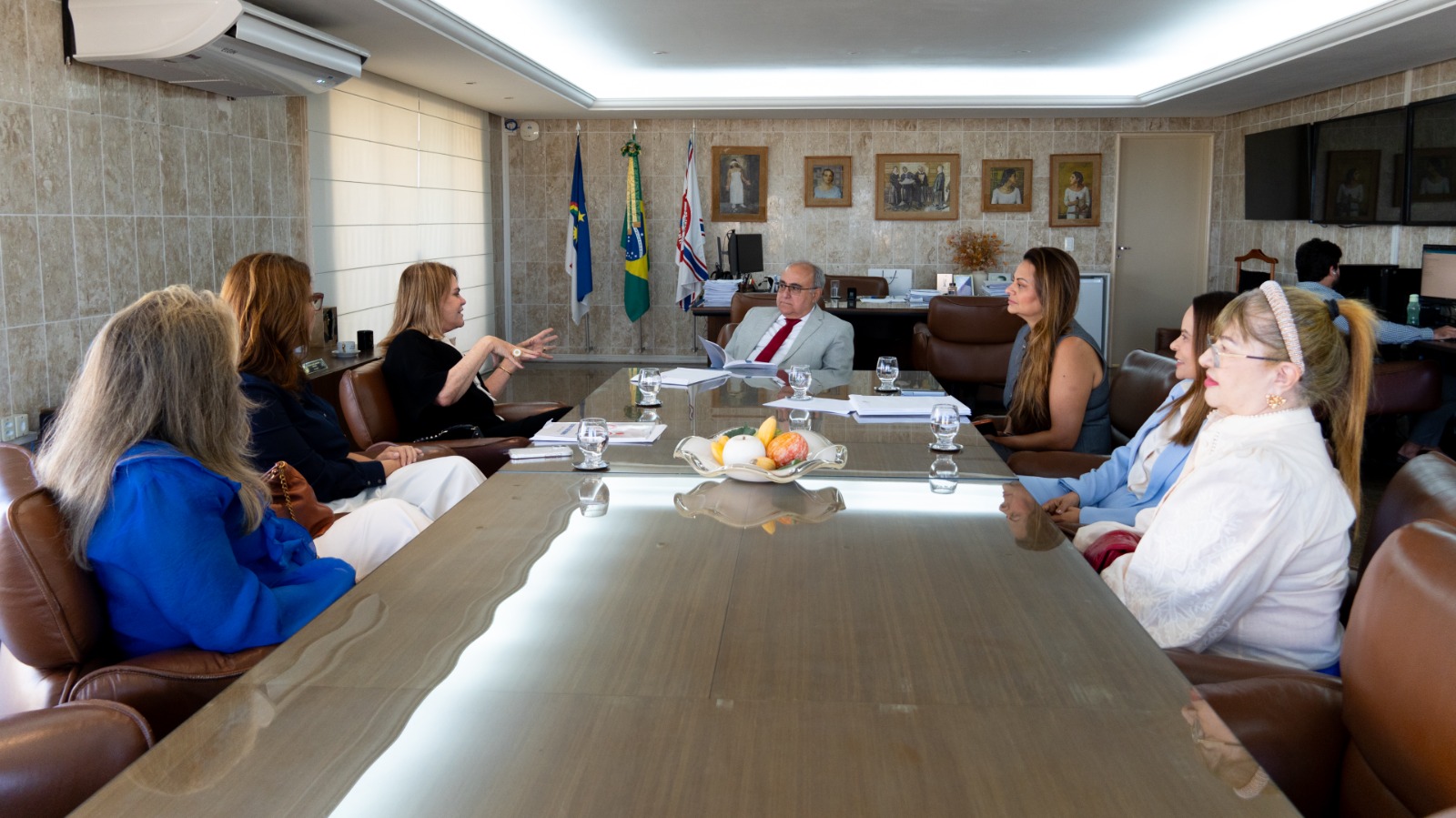 Corregedor sentado na ponta da mesa de seu gabinete, ladeado pelas diretoras da AAJUPE