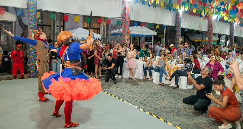 à esquerda, um casal vestido de cangaceiro se apresentando para as pessoas que estavam presentes no Arraiá do TJPE