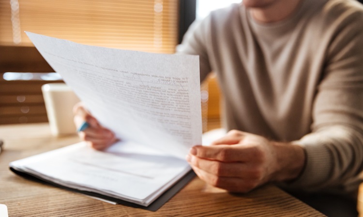 Pessoa sentada à mesa, lendo um documento documento que está segurando